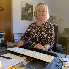 Petra Heine an ihrem Arbeitsplatz vor einem Computer und mit Headset ausgestattet