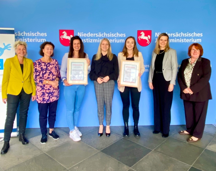 Vor der Pressewand stehen Frau Dr. Anja Meyer, Frau Prof. Dr. Ute Ingrid Haas, Frau Kim Oberstedt, die Niedersächsische Justizministerin Dr. Kathrin Wahlmann, Frau Theresa Kessen, Frau Susanne Wolter und Frau Kirsten Böök
